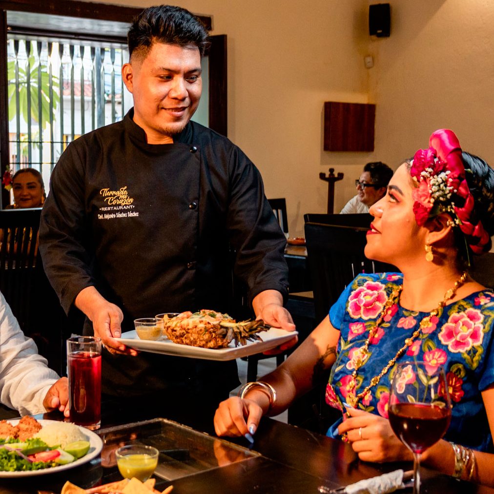 Nuestro chef sirve un platillo en piña a una comensal vestida de tehuana