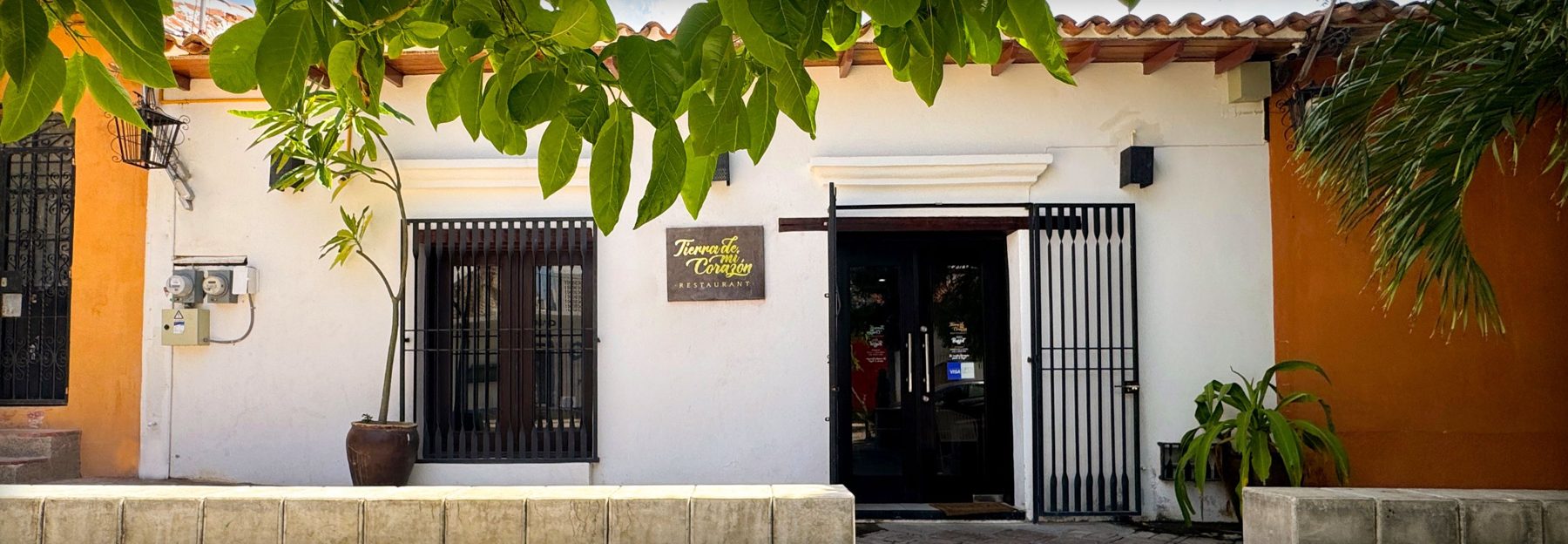 Fachada blanca del restaurante con su letrero y puerta negra