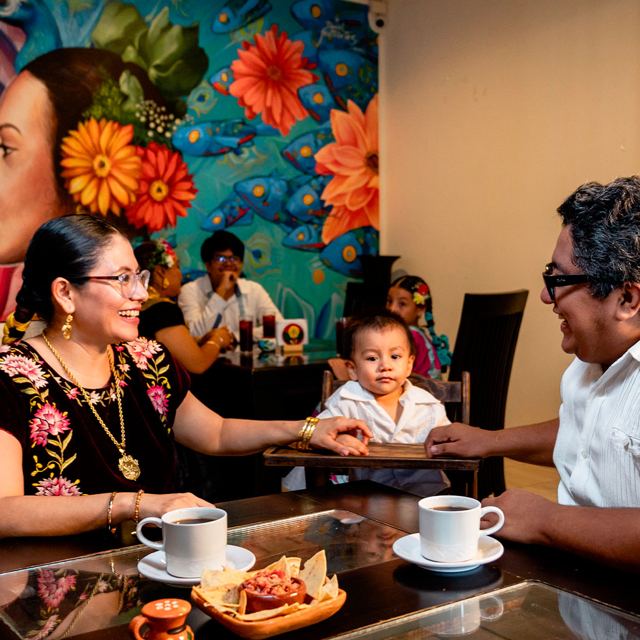 Una familia comparte café y totopos frente al mural del restaurante